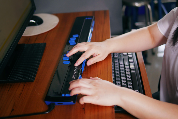 How to Make a Website Accessible - an image of a person using computer with braille display or braille terminal a technology assistive device for persons with visual impairment.